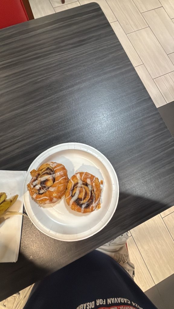 Two cinnamon rolls with icing on a disposable plate